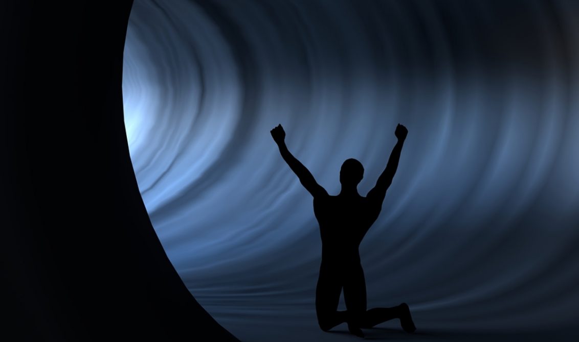 a man silhouette who raised his hands against the light in a tunnel