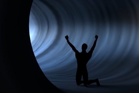 a man silhouette who raised his hands against the light in a tunnel